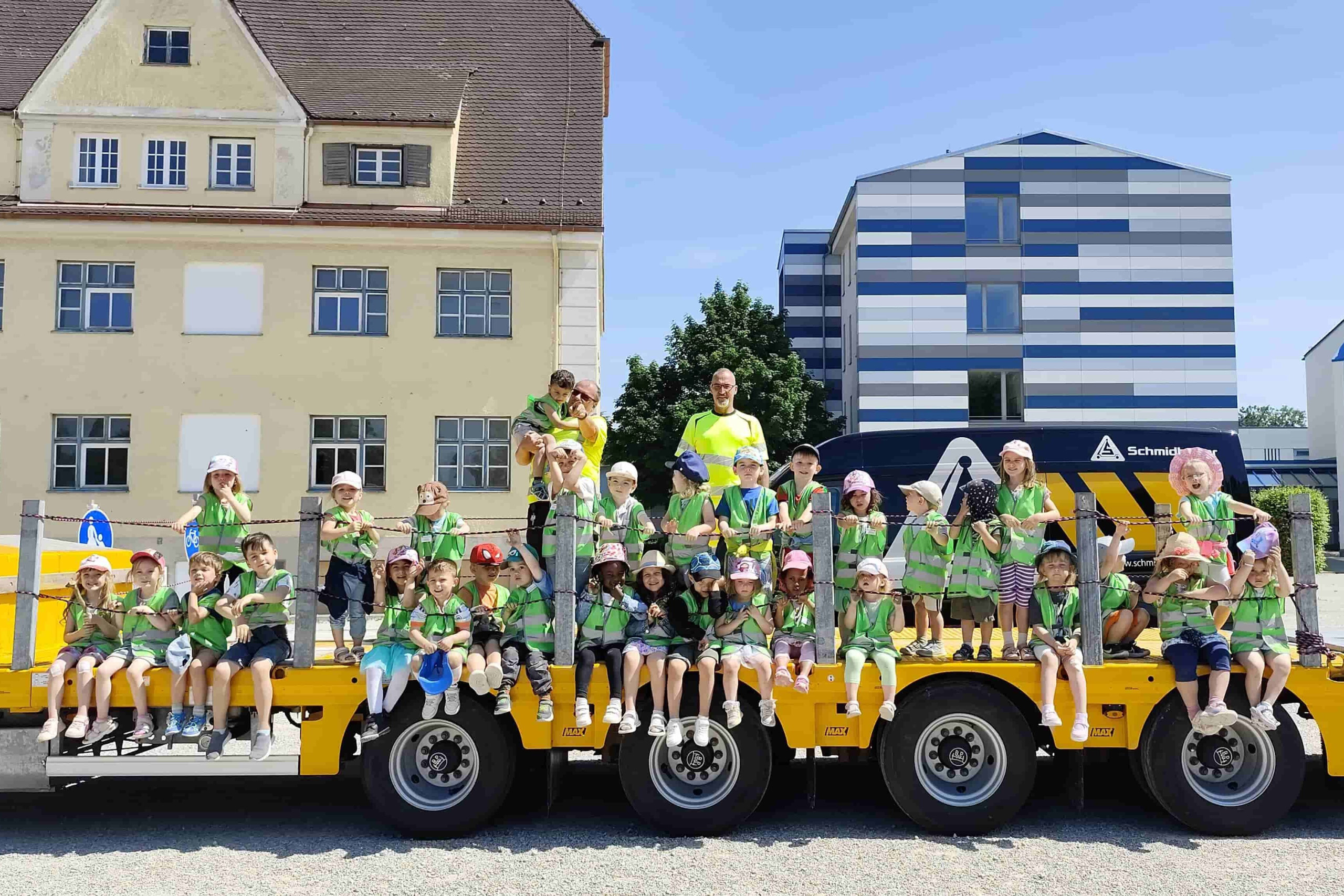 Kindergartengruppe mit SchFahrern und den Kindergarten-Pflegenden auf dem gelben Schmidbauer-Anhänger.